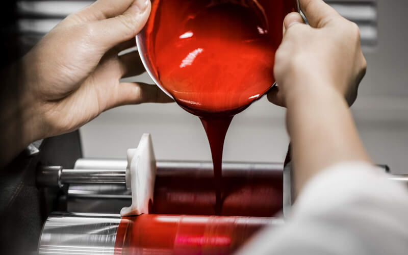 A technician pours a creamy preparation of red makeup into a machine