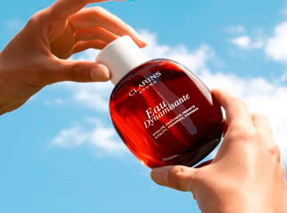 Zoom on two hands holding a Eau Dynamisante packshot with a sunny and cloudy sky in the background.