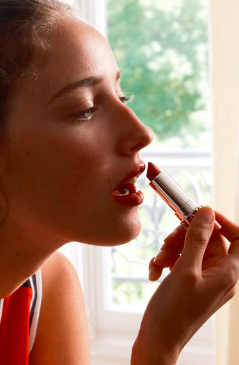 Young woman applying makeup in front of the mirror with a Joli Rouge lipstick